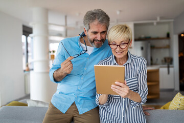 Happy smiling mature couple using digital tablet at home