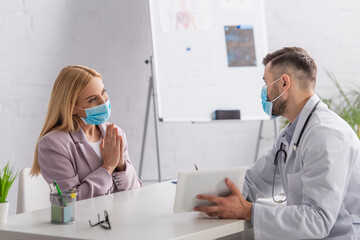 woman in protective mask showing please gesture near doctor with digital tablet