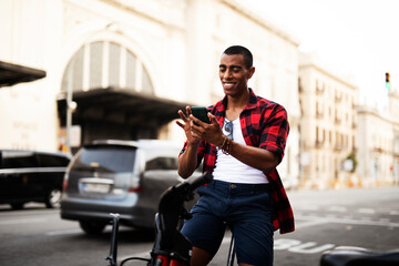 Portrait of handsome african man using electric bike in the city. Happy young man using the phone.