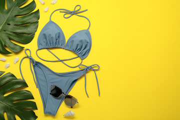 Stylish blue bikini, sunglasses and leaves on yellow background, flat lay. Space for text
