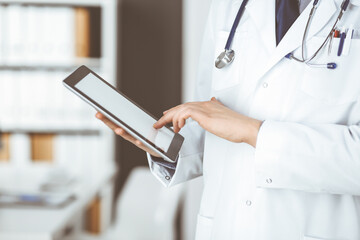 Unknown male doctor using tablet computer in clinic near his working place, closeup. Perfect medical service in hospital. Medicine and healthcare concept