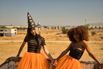 Portrait of young Hispanic and Latina women holding hands and leaning against a stone wall dressed for Halloween outside.