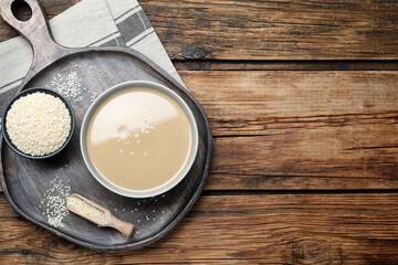 Tasty sesame paste and seeds on wooden table, top view. Space for text