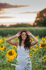 Portrait of a young beautiful woman with dark hair in a sunflower field at sunset. Happy. Summer.