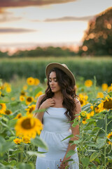 Portrait of a young beautiful woman with dark hair in a sunflower field at sunset. Happy. Summer.