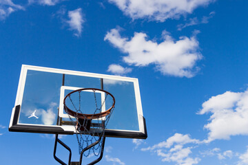 Naklejka premium Basketball ring against sunny blue sky with clouds