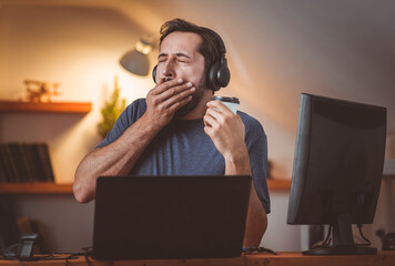 A middle-aged student yawns during class in the evening with headphones and coffee.