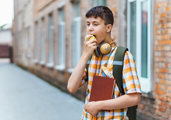 happy teen boy portrait on the way to school, he is eating an apple, education and back to school concept