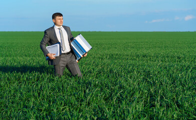 businessman poses in a green field, he goes with the documents and ladder, freelance and business concept, green grass and blue sky as background