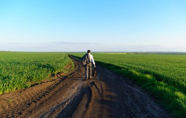 Fototapeta na wymiar businessman walks along a country road, green field, freelance and business concept, green grass and blue sky as background