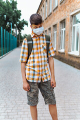 schoolboy poses in the backyard of the school, wearing a protective mask on his face from a coronavirus infection, education and back to school concept