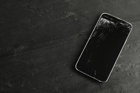 Top view of smartphone with cracked screen on black table, space for text. Device repair