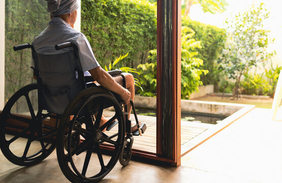 Old Asian Male With Cancer Wear Sitting On Wheelchair, She Feeling Lonely And Depress, She Look At Window And Hope To See Family, Elderly Healthcare.