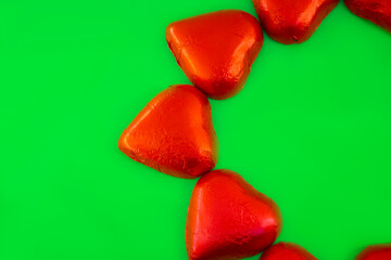 Chocolate candies shape of hearts on green background