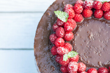 Chocolate cake with raspberries, on a white background of boards.