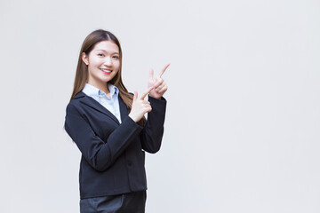 Asian working female who has long hair wears black formal suit with blue shirt while she shows point up to present something on white background.