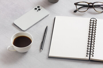 Blank notepad, mobile phone, glasses, coffee cup on the work table. 