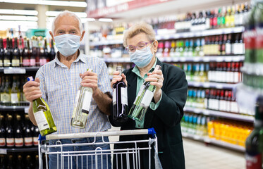 mature european spouses chooses bottle of wine in alcohol section of supermarket