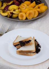 A sandwich with fish and fruits apricots, nectarines, cherries on a large plate on the table in the morning during breakfast.