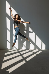 Asian dancer girl makes an acrobatic jump illuminated by the sun that enters through the window in an empty building