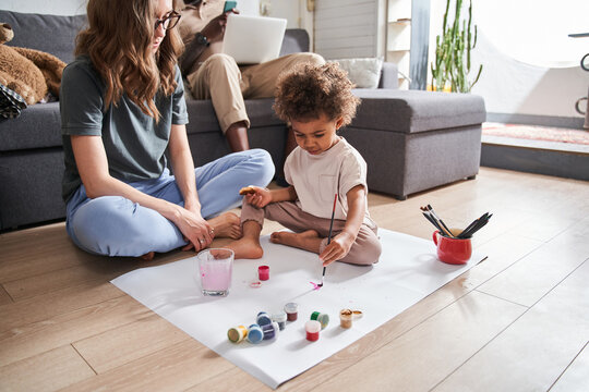 Girl drawing hand made picture with her mother while sitting at the floor together