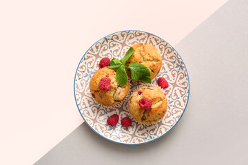 Plate with tasty raspberry muffins on color background