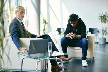 Mature mental health professional uses laptop while having counselling with black teenage boy.