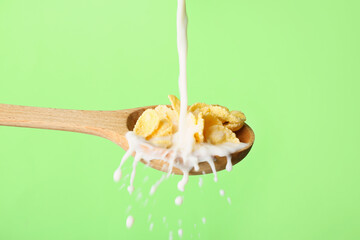 Pouring of milk into spoon with cornflakes on color background, closeup