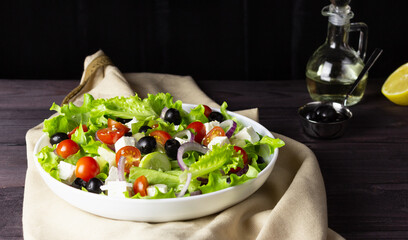 Greek salad in a plate on a dark background. Healthy vegetarian food. Feta cheese, lettuce leaves, cherry tomatoes.