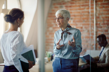 Mature executive director communicates with her junior associate while working at corporate office.