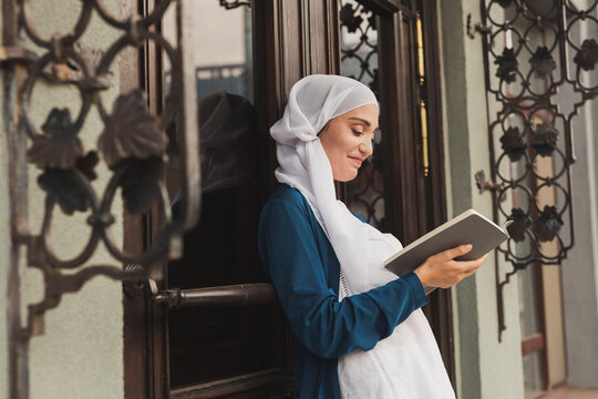 Portrait of young muslim woman wearing hijab reading book outdoors
