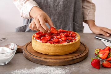 Obraz na płótnie Canvas Woman decorating tasty pie with strawberry at table in kitchen, closeup