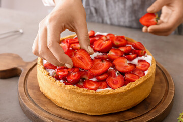 Obraz na płótnie Canvas Woman decorating tasty pie with strawberry at table in kitchen, closeup
