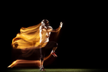Portrait of young man, American football player training isolated on dark studio background with mixed neon light. Concept of sport, competition and beauty