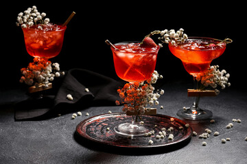 Glasses with tasty cocktail and beautiful gypsophila flowers on dark background