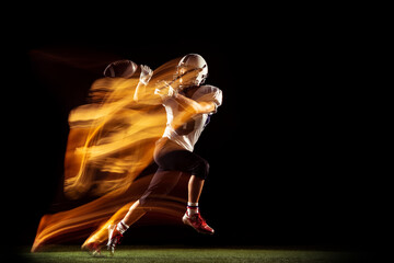 Portrait of young man, American football player training isolated on dark studio background with mixed neon light. Concept of sport, competition and beauty