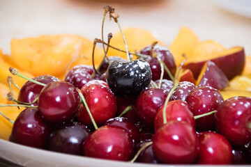 Fruits apricots, nectarines, cherries on a large plate on the table in the morning during breakfast, close-up