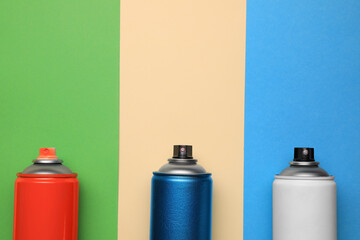 Cans of different spray paints on color background, flat lay with space for text. Graffiti supplies