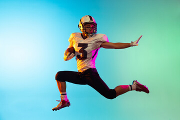 Obraz premium Portrait of American football player catching ball in jump isolated on blue studio background in neon light.
