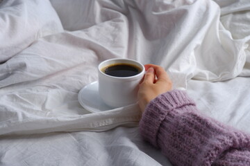 Girl holding a cup of coffee in bed. Breakfast in bed. Interior. Cosiness.