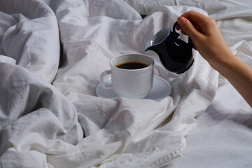The girl pours milk into a cup of coffee. Breakfast in bed. Interior. Cosiness.