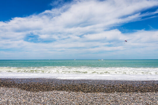 Beautiful empty pebble stone beach in Batumi, Georgia. Boat with paragliding. Bright Summer sunny day, blue water. No people.