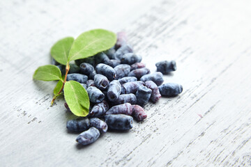 Honeyberry or haskap berries with fresh green leaves on grey wooden background