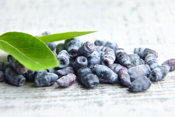 Honeyberry or haskap berries with fresh green leaves on grey wooden background