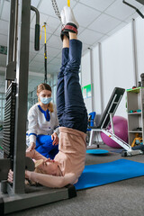 Female doctor rehabilitologist working with female patient on the special rehabilitation device