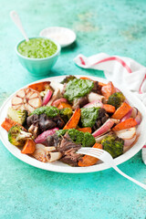 Grilled lamb legs meat on the bone with pesto or chimichurri sauce and baked vegetables - sweet potatoes, onions, broccoli and garlic, selective focus