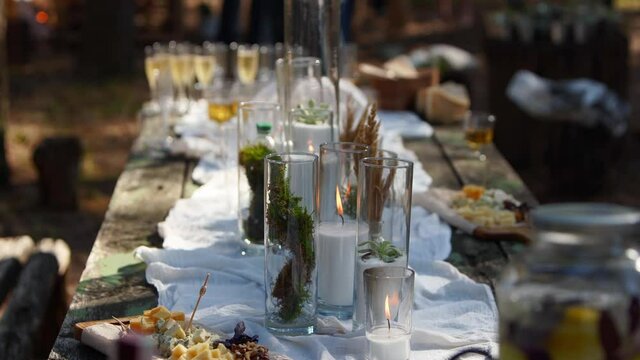 Person takes cheese from dining table decorated in boho style with candles, cloth, flowers, served with tableware, dishes, meals, stemware, drinks. Wedding party banquet catering outdoors in forest.