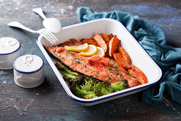 Baked sockeye salmon fish fillet with roasted sweet potato and broccoli, in enameled baking dish,...