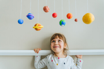 Little girl playing with toy planets made by herself from colorful molding clay indoor