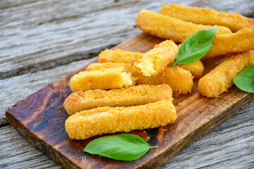 Vegetarian cheese breaded  oven baked  mozzarella sticks with  fresh basil on wooden background 